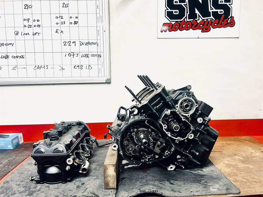 Engine stripped down on the workshop bench with cam timing figures on the board